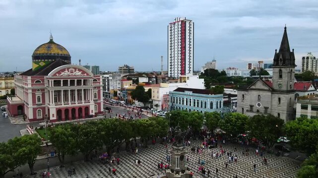 Main square at Teatro Amazonas in Manaus, Brazil. Large crowds of people fill the area during a cloudy afternoon. Static aerial next to historic fountain in 4K.