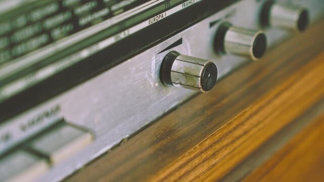 Close view of fingers rotating volume knob on retro radiogram audio system. Suitable for analog sound control, vintage electronics and broadcasting visuals.