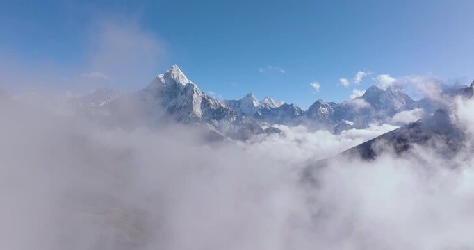 Aerial shot passing through clouds reveals the Khumbu snow-capped mountain landscape and Ama Dablam peak in the Everest region of Nepal with dramatic Himalayan scenery.