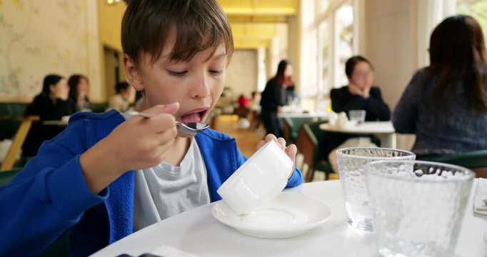 Hungry young boy enthusiastically finishes his meal, using tablespoon to scrape very last drops of soup from empty bowl. Candid close-up capturing child's healthy appetite and pure satisfaction