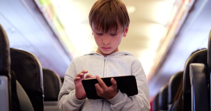 Candid handheld shot of young boy standing in airplane aisle, deeply absorbed in productivity app on his tablet. Real-life moment of focused 'future boss' staying productive and tech-savvy