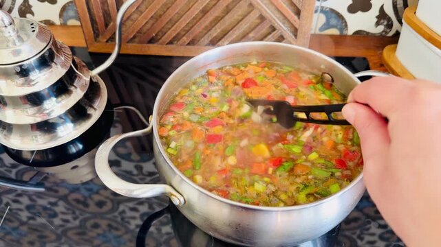 Traditional vegetable soup Chorba in a pot on a luxury kitchen with oriental tile. Healthy Halal meal for Ramadan Iftar. Authentic Asian cuisine cooking process in a stylish home interior.