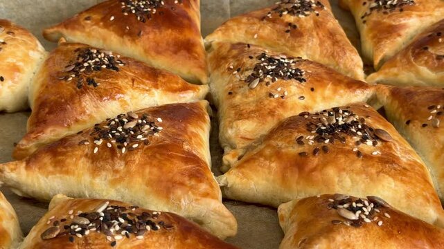 Freshly baked golden meat samsa on a tray for Ramadan Iftar. Traditional puff pastry with sesame, flax, and pumpkin seeds. Delicious Halal food for breaking the fast, Ramadan Kareem, homemade.