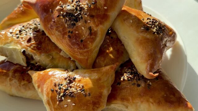 A plate of fresh golden meat samsa with sesame and nigella seeds for Ramadan Iftar. Traditional Asian puff pastry triangles, delicious Halal food for breaking the fast, Ramadan Kareem.