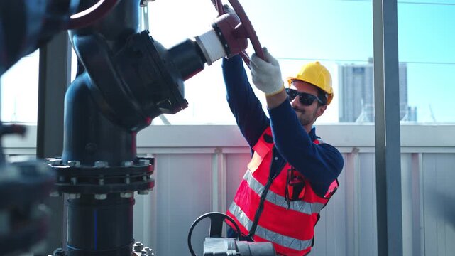 Young male engineer inspecting industrial pipeline systems while communicating via walkie talkie and recording data on a tablet, representing professional infrastructure management