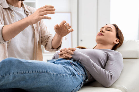 Male psychologist with pendulum hypnotizing woman on couch in office