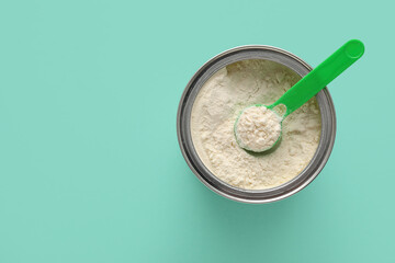 Obraz premium Jar of powdered baby milk formula with measuring scoop on turquoise background
