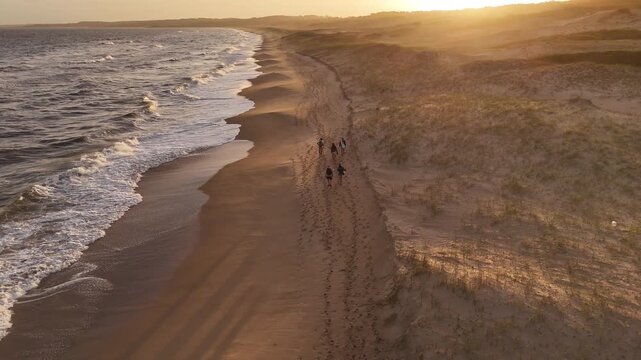 Drone shot follows tourists walking on Playa del Barco beach on the Atlantic Ocean during sunset in Santa Teresa Park.