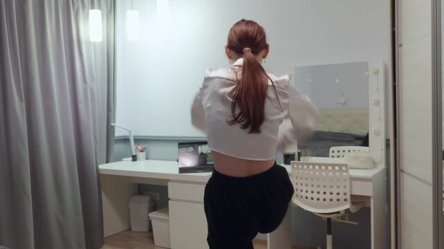 A talented teenage girl with long hair performs a contemporary dance routine in her modern bedroom. She moves with grace and passion, her reflection visible in the mirror.