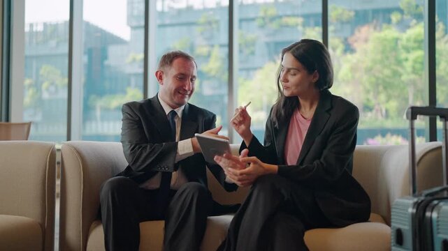 Two business professionals signing a digital document on a tablet with a stylus and shaking hands to finalize a business deal in a modern high-rise office lounge