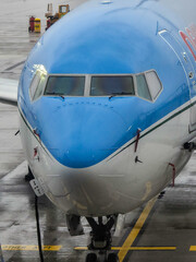 Close up of a modern commercial airplane nose and cockpit windows at a rainy airport apron.