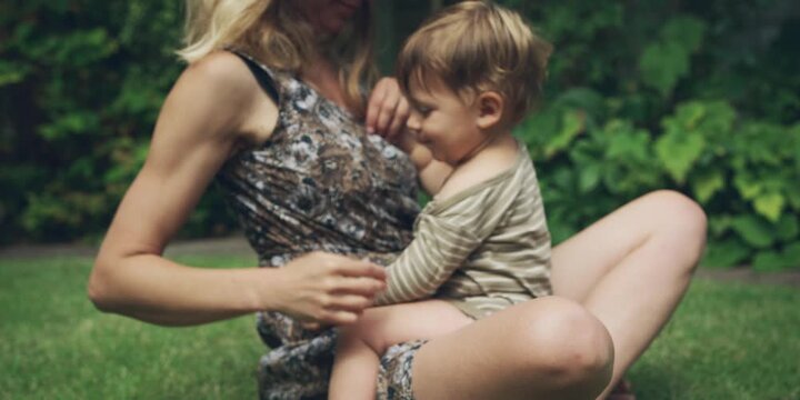 Woman with blonde hair sitting on the grass holding a toddler in her lap