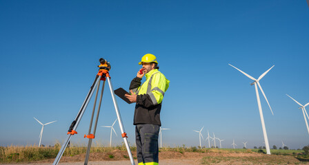 Engineer wearing uniform inspection and survey work in wind turbine farms rotation to generate electricity energy. Maintenance engineer working in wind turbine farm at sunset.