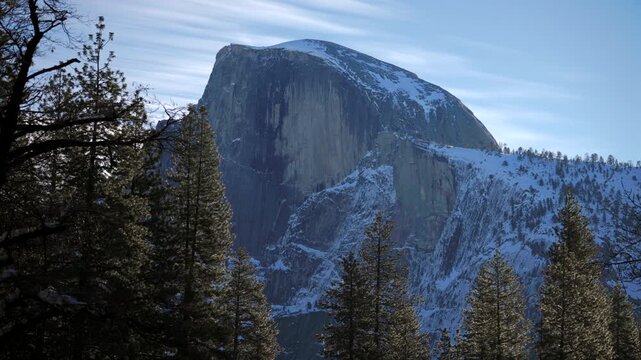 Snowcapped half dome in Yosemite National Park framed by pines granite monolith rises above timbered ridgeline crisp sky and distant snowy slopes convey solitude, winter landscape