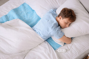 Young man sleeping on electric heating pad in bedroom, top view © Pixel-Shot