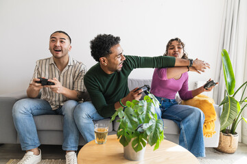 Diverse group of young friends having fun and competing playfully while sitting on a couch gripping controllers and gaming together © Koldo_Studio