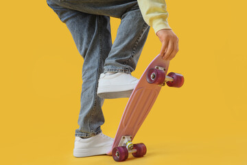 Legs of young man with skateboard on yellow background, closeup © Pixel-Shot