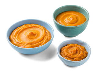 three bowls of vibrant orange pumpkin puree or butternut squash soup, artfully swirled and served...