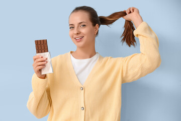 Young woman with chocolate bar on light blue background