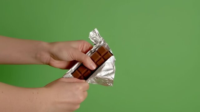Hands opening a foil-wrapped chocolate bar on a green background