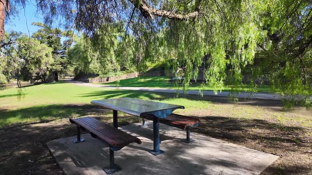 Picnic table and bench under leafy trees in a quiet suburban park in Melbourne, Australia. Shaded green space with walking trail and peaceful natural environment. Outdoor recreation and relaxing 