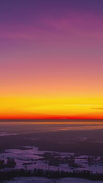 Vertical lateral tracking hyperlapse revealing dramatic orange sunset sky above snowy countryside and forests with low clouds and distant horizon in winter landscape Latvia