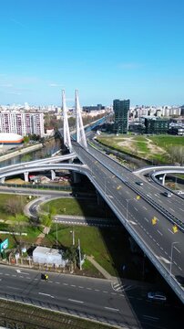 Aerial drone view of Ciurel Bridge and Lacul Morii area in Bucharest, Romania, showing urban roads, modern bridge infrastructure, nearby residential district and lake under clear blue sky