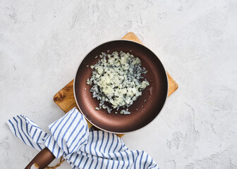 Cooking onions in a frying pan on a wooden cutting board in a kitchen setting during the day