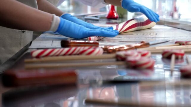 Close-up of a variety of different caramel candies on sticks in a handmade candy shop, with chefs rolling out soft caramel in the background.