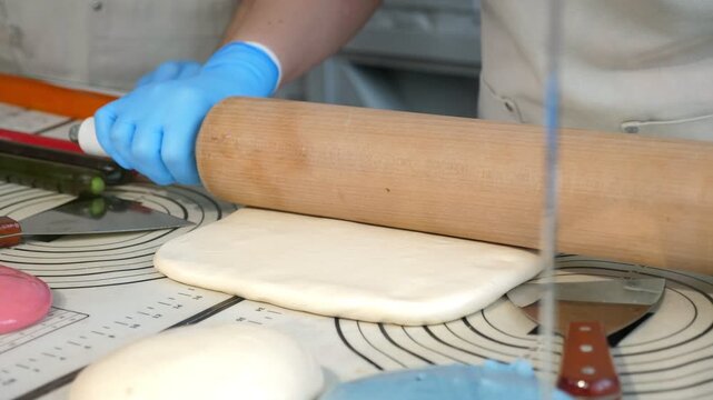 Close-up of two pastry chefs making homemade lollipops in a professional pastry shop. They roll out soft caramel using a rolling pin and their hands.