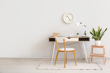 Interior of stylish room with workplace, houseplant, lamp and clock hanging on white wall