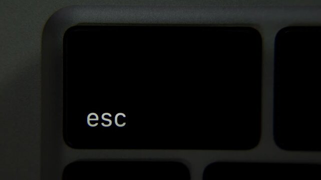 Esc label on a laptop key lights up as backlight activates the symbol in a close view of a computer keyboard. User interface, technology workflow.