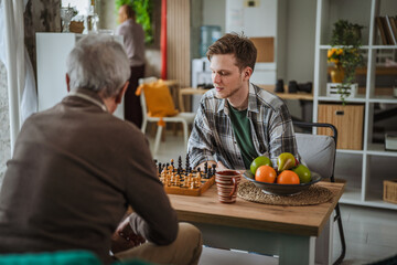 Fototapeta premium Young generation man playing chess with senior person