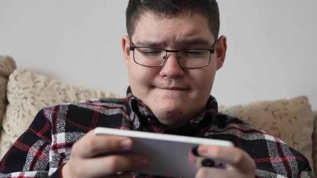A teenager plays on a smartphone while sitting at home, focused on the screen.
