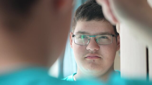 teenager in glasses combs his hair in front of a mirror,