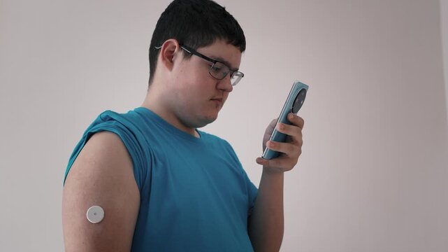 A teenager checks his blood sugar level using a smartphone and a continuous glucose monitoring system.