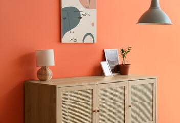 Fototapeta premium Chest of drawers with lamp, magazine and houseplant near orange wall in living room, closeup