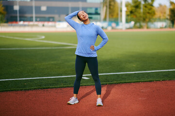 Fototapeta premium Young asian woman stretching neck muscles before workout on sports field