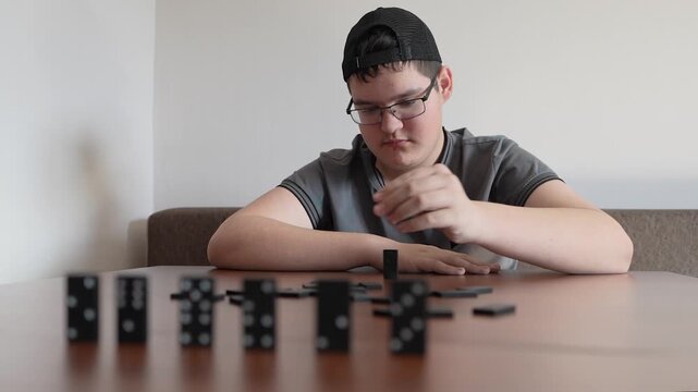 A teenager plays dominoes sitting at a wooden table, focused on the game.