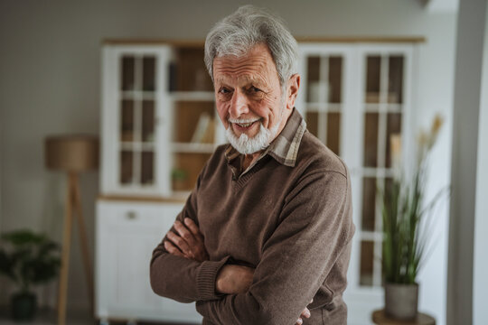 Senior man with white beard crossing arms at home