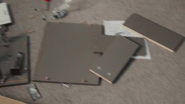 Handheld no people shot, filmed with digital camcorder of components of flatpack drawer scattered on carpet in living room at family home during assembly, tools, fixtures, hardware, instruction manual