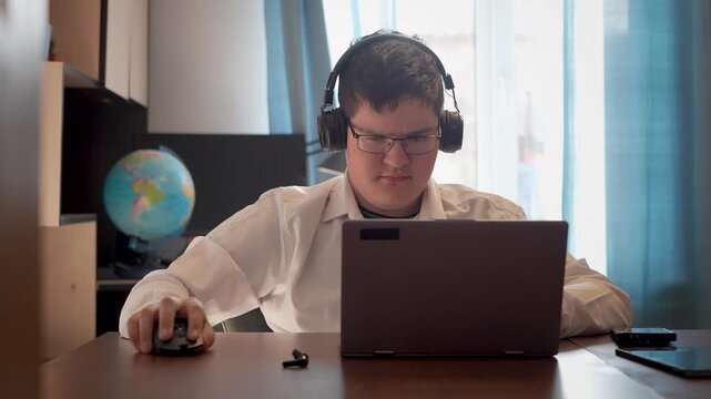 A teenage boy plays or works on a laptop while sitting at home. Remote learning is a concept. A teenager is typing on keyboards.