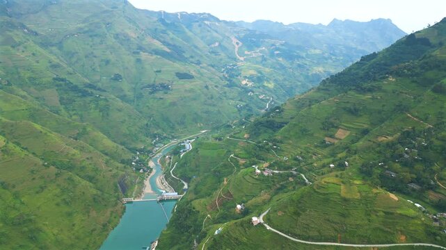 Stunning aerial footage of the Nho Que river canyon. High angle view of the vibrant green mountains, terraced fields, and a dam