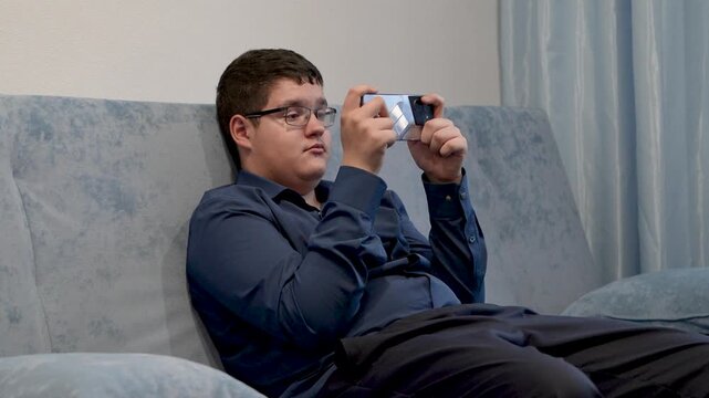 A teenager in glasses looks at his smartphone with surprise, reacting to an unexpected message or shocking online content.