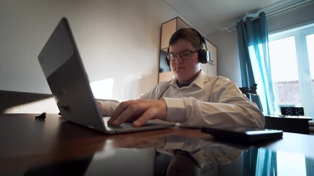 A teenage boy plays or works on a laptop while sitting at home. Remote learning is a concept. A teenager is typing on keyboards.