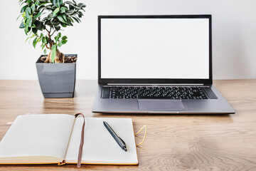 Minimal home office workspace with laptop mockup screen and notebook with pen on wooden desk. Modern remote work, freelancer planning and productivity concept with copy space
