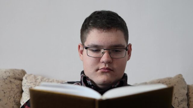 A thoughtful teenager holds the back of his head while reading a textbook, deep in concentration.