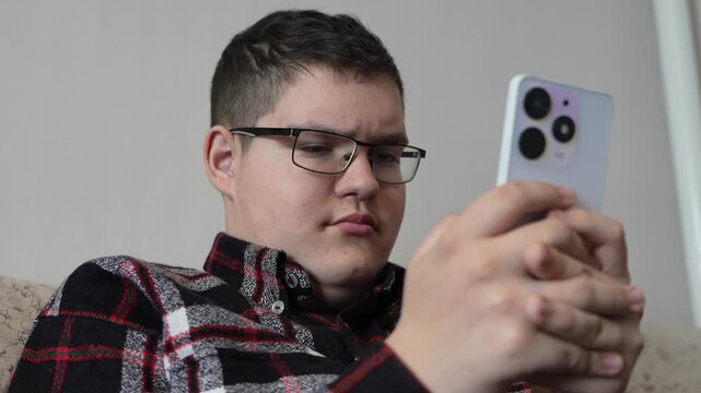 Caucasian teen boy texting on smartphone at home. A focused teenager fiddles with his smartphone while browsing messages or content on the Internet.