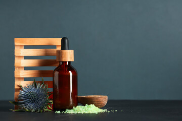 Beautiful spa composition with heap of sea salt, flower and bottle of cosmetic product on grey...