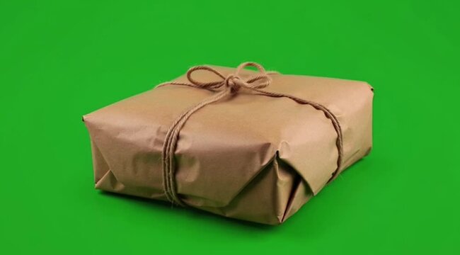 A carefully wrapped brown paper parcel tied with twine rotating on green screen background